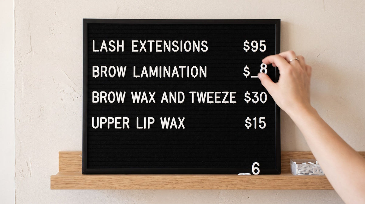 A black felt letterboard salon price list with a hand replacing one of the price tiles, the old number resting on the shelf below.